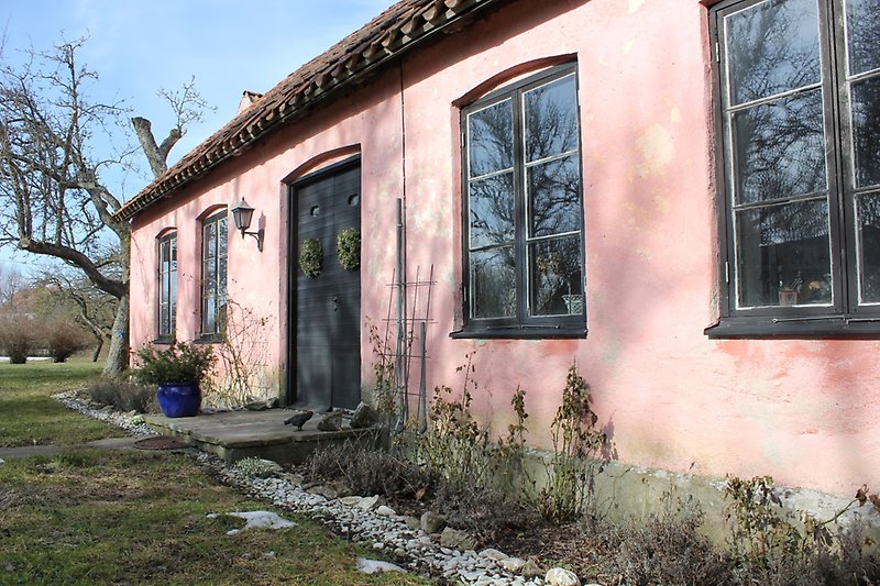 Ett litet rosa hus med svarta fönster och en svart ytterdörr.