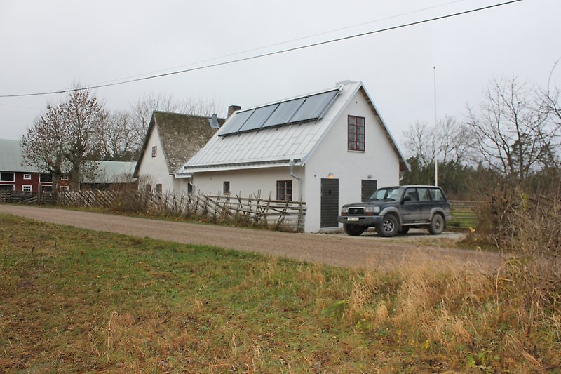 Ett vitt hus med bruna fönster, svart ytterdörr och ett plåttak.