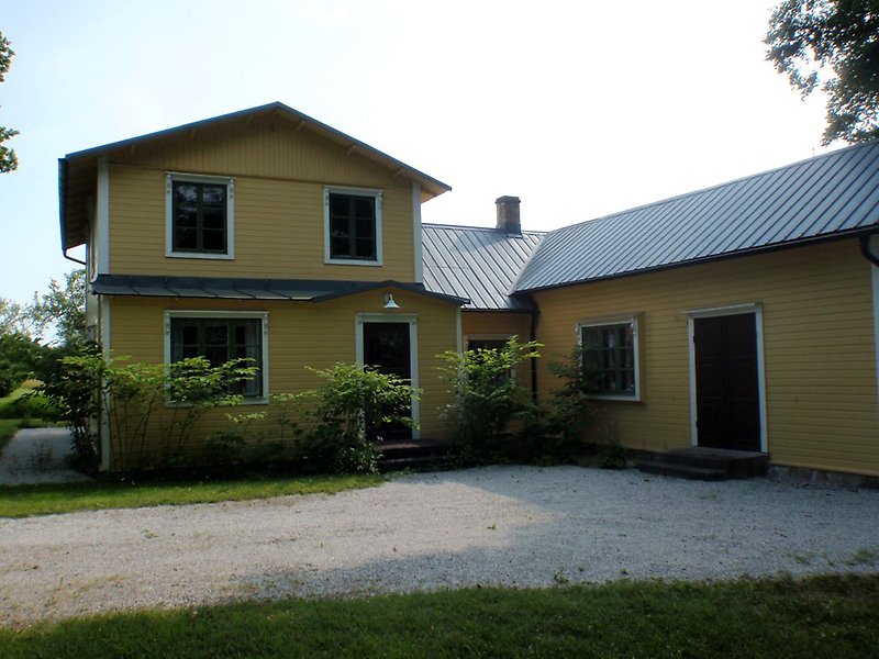 Ett gult trähus med gröna fönster och en svart ytterdörr.