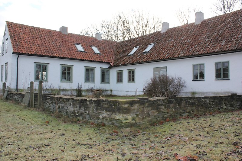 Ett vitt hus med gröna fönster, fyra skorstenar och ett rött tak.
