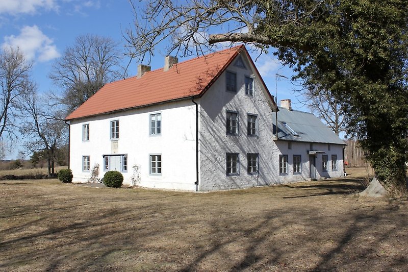 Ett vitt hus med gråa dörrar, gråa fönster och ett plåttak.