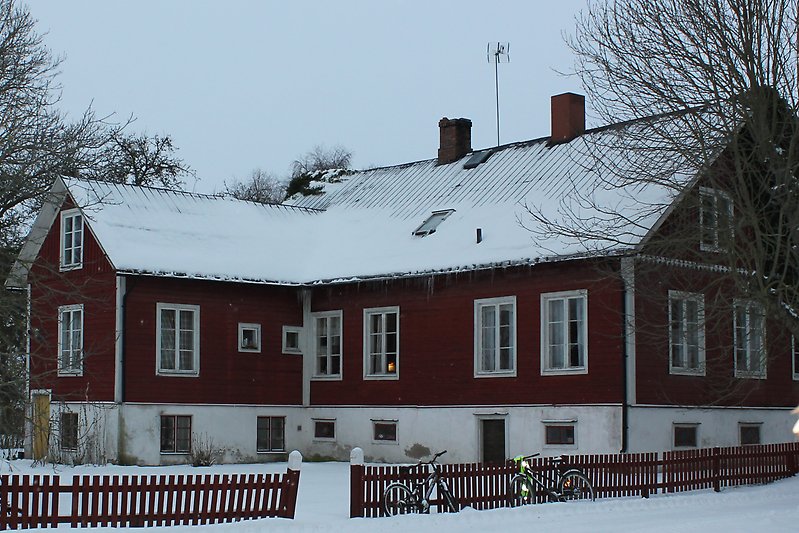 Ett rött hus med en träfasad, vita fönster och ett plåttak.