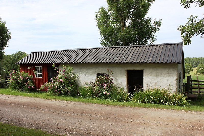 En liten rödvit byggnad med ett svart plåttak längs grusvägen.