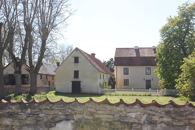 Bakom stenmuren finns det tre ljusgula hus svarta fönster.
