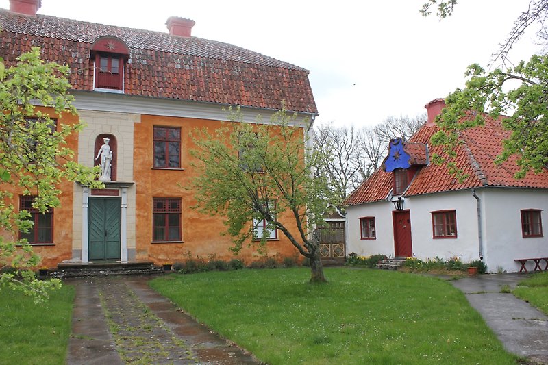 Ett vackert orange hus med röda fönster, en grön ytterdörr och ett rött tak.