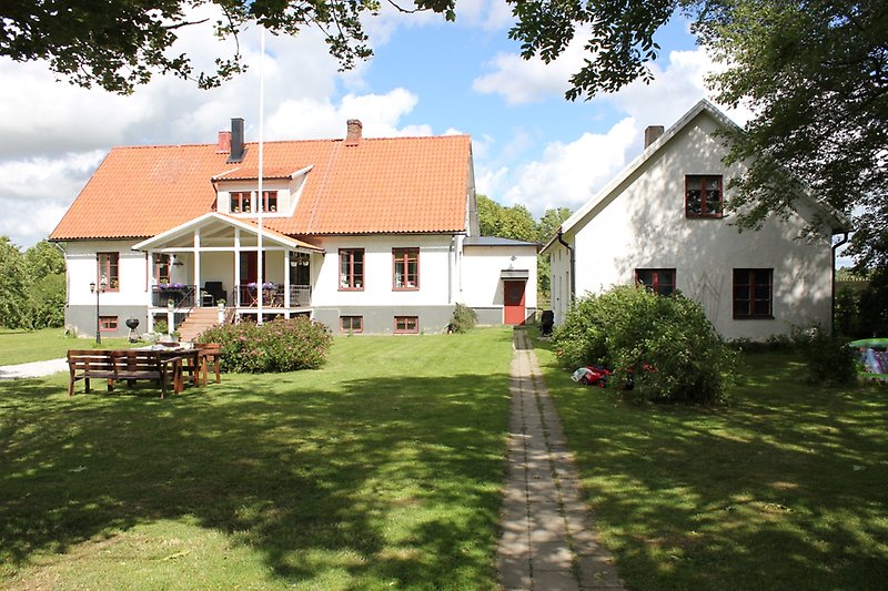 Ett vitt hus med en röd ytterdörr, bruna fönster och ett brunt tak med två skorstenar.