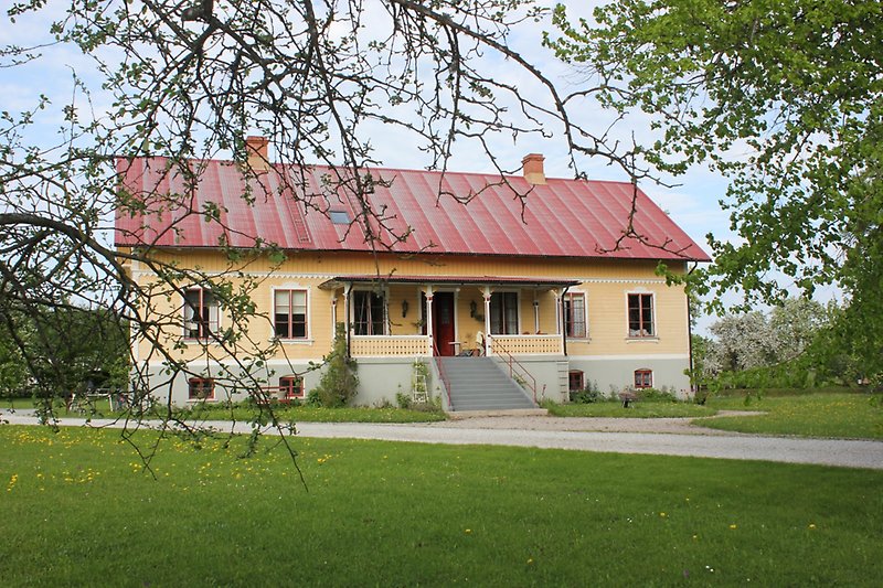 Ett gult hus med rött tak, två skorstenar, bruna fönster och en brun ytterdörr.