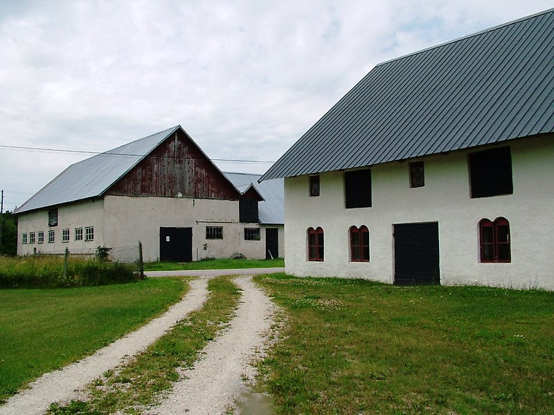 En vit byggnad med svarta dörrar, röda fönster och ett plåttak.