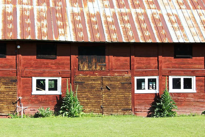 En röd lada med ett rostigt plåttak och små vita fönster.