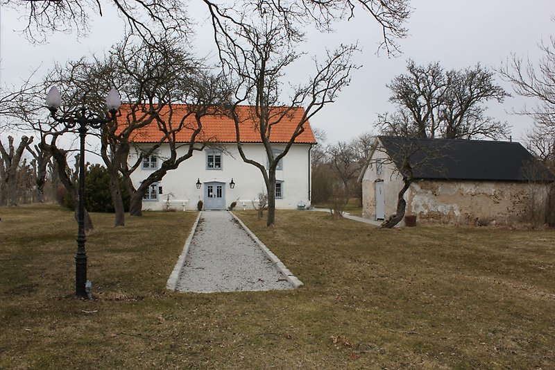 Ett vitt tvåvåningshus med gråa dörrar, gråa fönster och ett rött tegeltak.