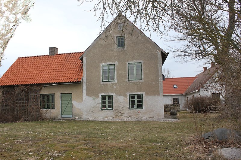 Ett hus med gröna fönster, grön ytterdörr, ett rött tak och en skorsten.