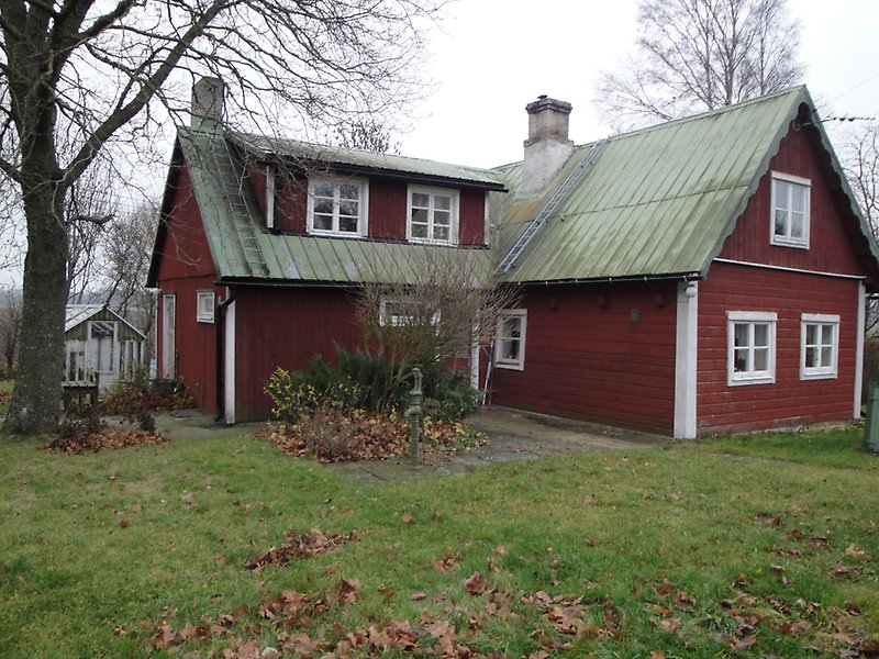 En röd trästuga med vita fönster och ett grönt plåttak med två skorstenar.
