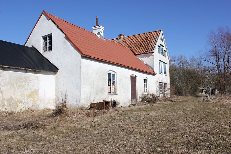 Ett vitt hus med ljusblåa fönster och ett tegeltak med två skorstenar.