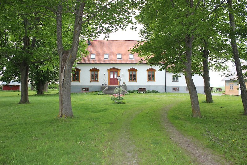 Ett vitt hus av en våning med ett rött tak, röda fönster med gula fönsterramar och en röd ytterdörr.