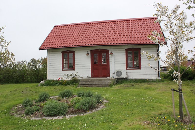 En vit trästuga med rött tak, röda fönster och en röd dörr.