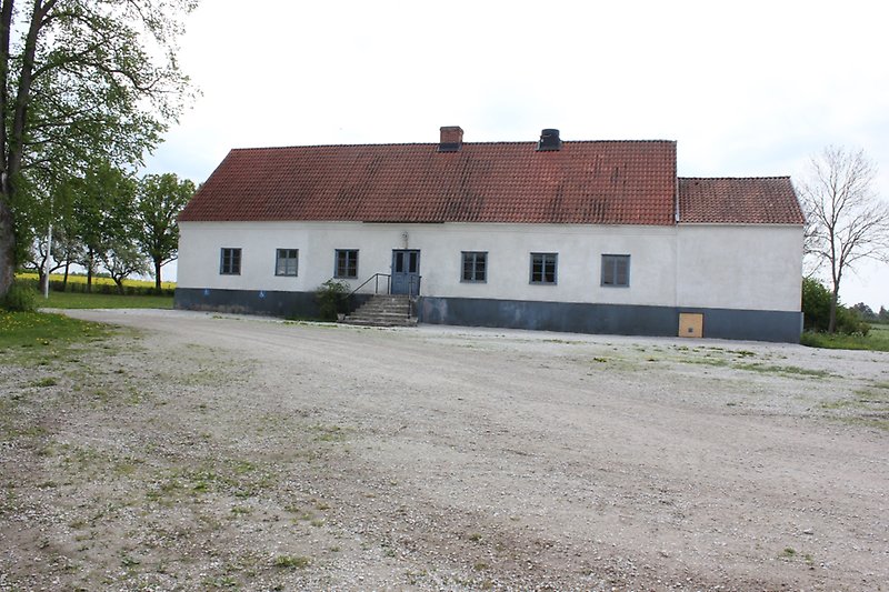 En vit envåningsbyggnad med blåa fönster, blåa dörrar och ett rött tegeltak med en skorsten.