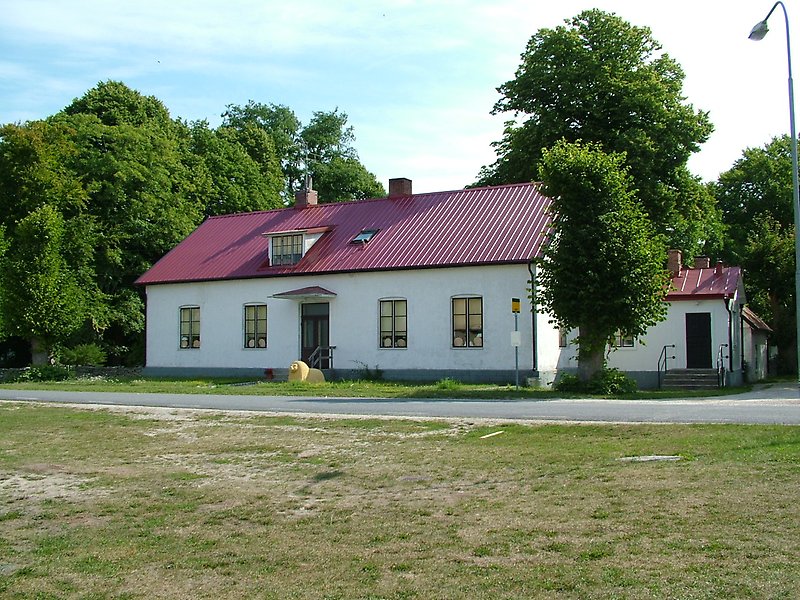Längs vägen och precise bakom en busshållplats finns det en vit envånings skolbyggnad med ett rött plåttak.