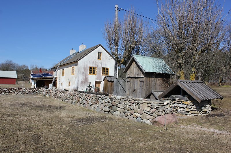 Bakom den låga stenmuren ser man solceller, och till höger om dem står det ett vitt tvåvåningshus med gula fönster.