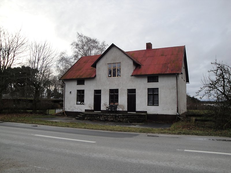 En tvåvåningsbyggnad med putsade väggar, svarta fönster, svarta dörrar och ett rött plåttak.