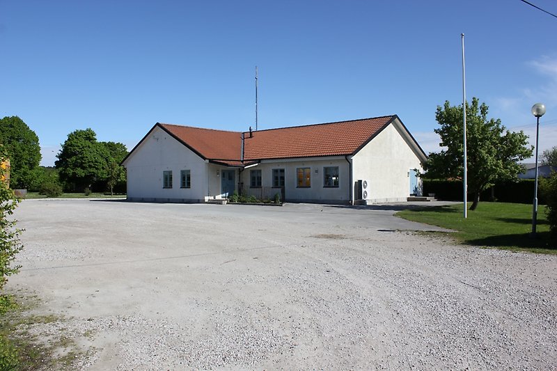 En vit envånings byggnad med putsade väggar, blåa dörrar, blåa fönster och ett rött tegeltak.