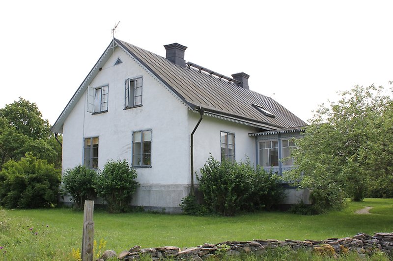 Ett vitt tvåvåningshus med ljusblåa fönster och ett grått plåttak.