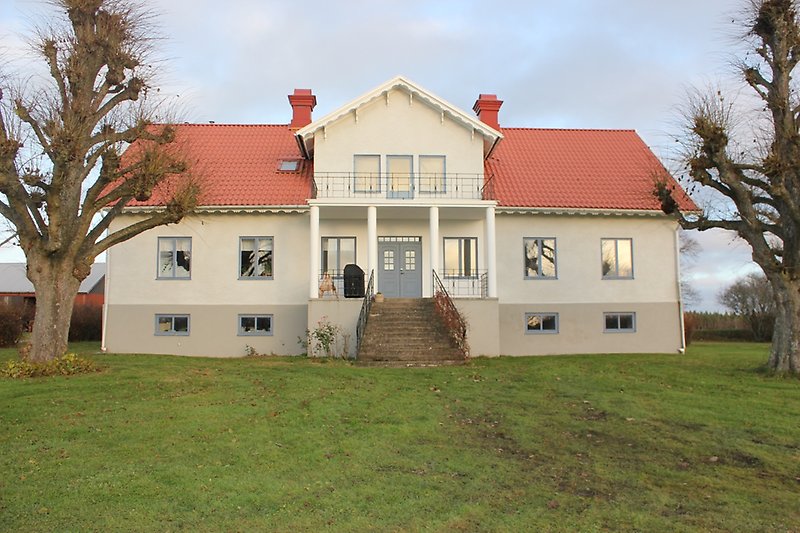 Ett gråvitt hus med blåa fönster, en blå ytterdörr och ett rött tegeltak.