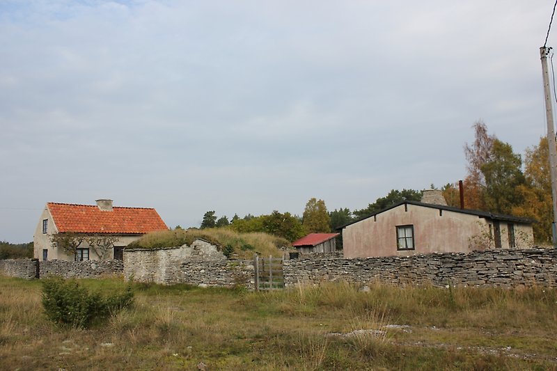 Bakom en liten stenmur finns det ett hus och flera andra mindre byggnader.
