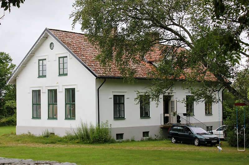 En vit envåningsbyggnad med stora gröna fönster och ett rött sadeltak med två skorstenar.