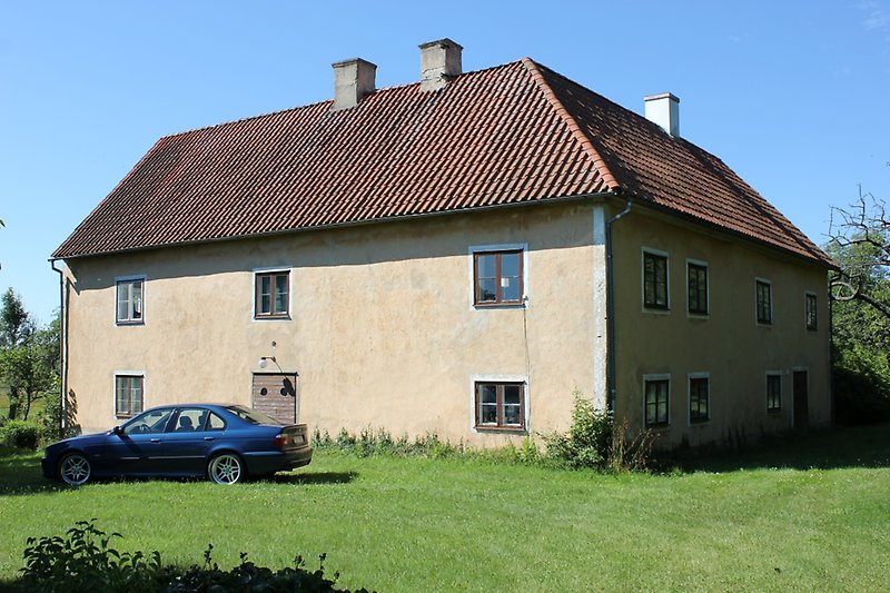 Ett stort ljusbrunt tvåvåningshus med bruna fönster och ett brunt tegeltak med tre skorstenar.