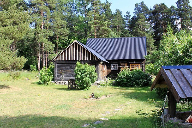 En svart trästuga med vita fönster och ett svart plåttak.