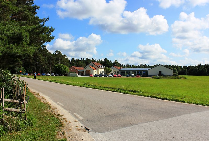 På höger sida om vägen finns det några byggnader och tiotals parkerade bilar.